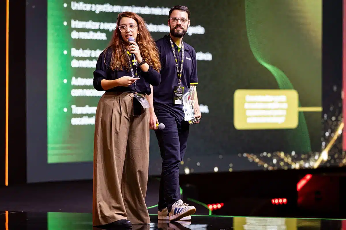 Nathalia Freitas apresenta o projeto da Plataforma Mid ao lado de André Reichelt, que segura o troféu do Falconi Awards 2026.